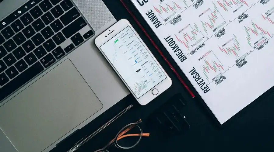Laptop, smartphone, and financial charts on office desk for market analysis.