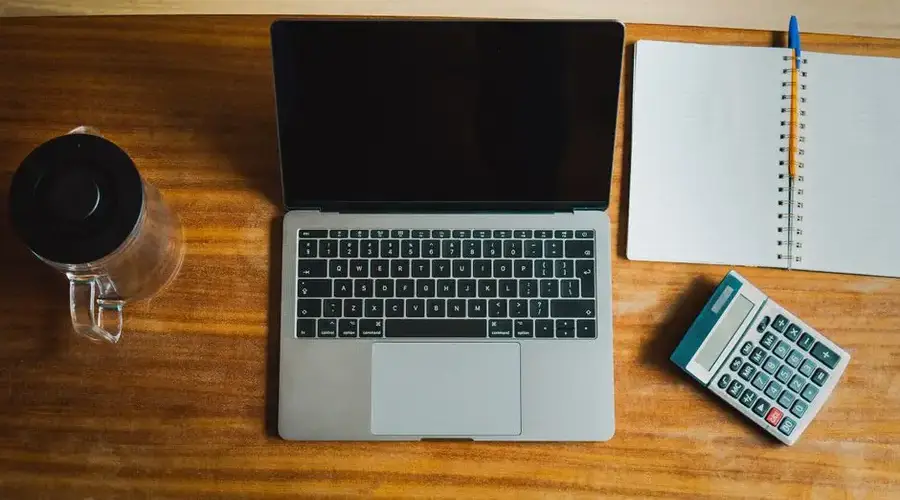 Flat lay of workspace featuring a laptop, calculator, and notebook on a wooden desk.