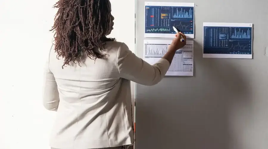 A businesswoman in a suit presenting financial data on charts during a meeting.