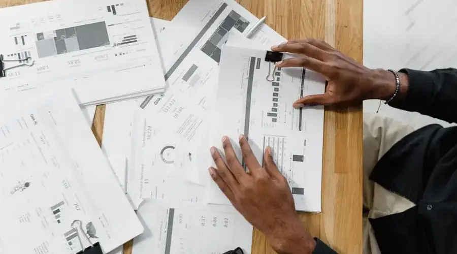 Top view of a professional reviewing financial documents at a wooden workspace.