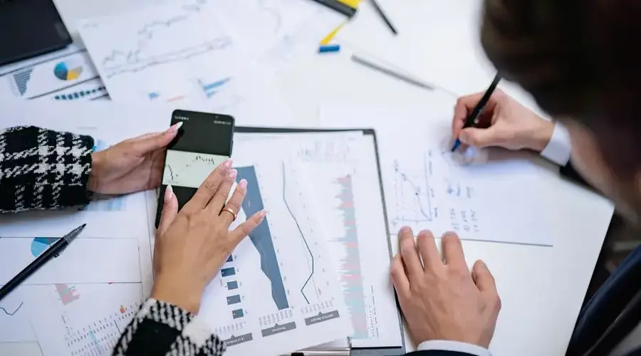 Overhead view of people analyzing financial graphs and data with smartphone and documents.
