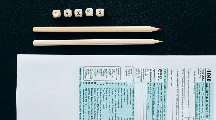 Flat lay of 1040 tax form with pencils and 'TAXES' blocks on black background.