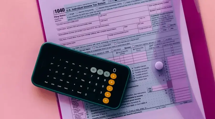 Tax form 1040 with a calculator on a pink background, highlighting finance and accounting themes.