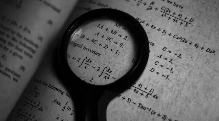 A magnifying glass focuses on mathematics formulas in a book, enhancing study and exploration.