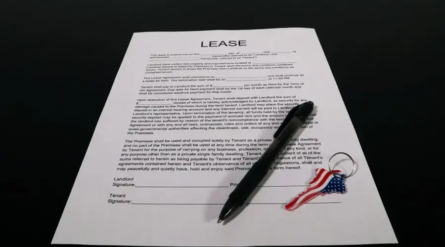 Lease agreement document with pen and American flag keychain on a black table.