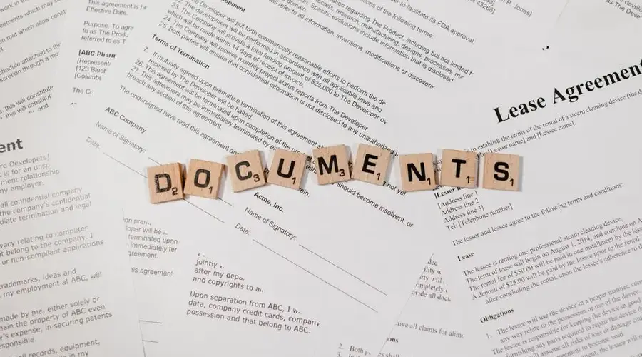 Top view of scrabble tiles spelling 'DOCUMENTS' on various contracts and agreements.