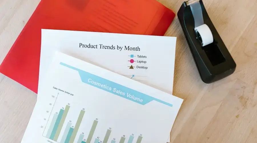 Top view of a desk with sales reports, a red folder, and a tape dispenser, ideal for business and office themes.