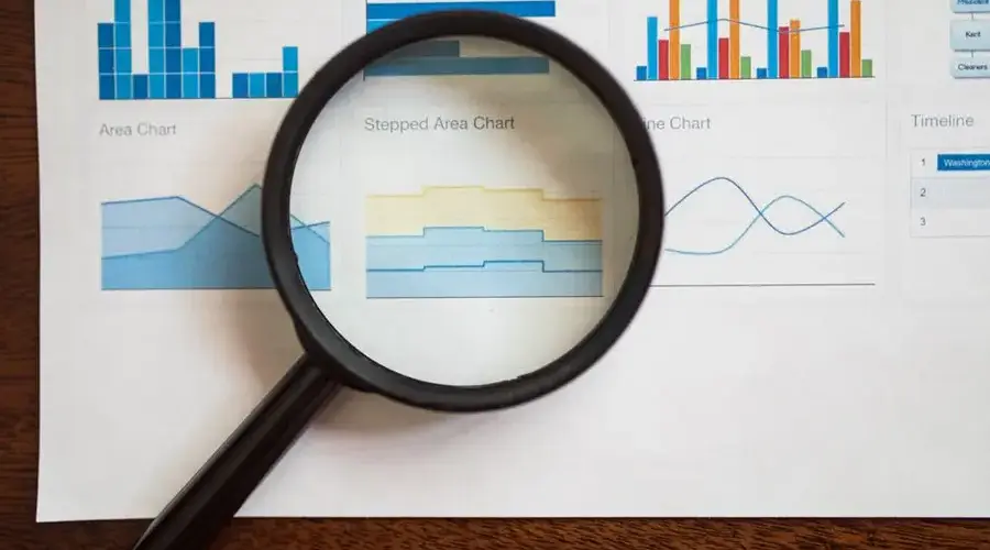 A magnifying glass focuses on various business charts and graphs on paper.