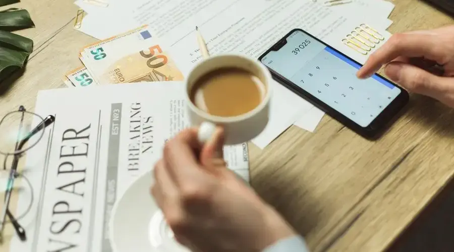 High-angle view of a business workspace with documents, coffee, currency, and smartphone calculator.