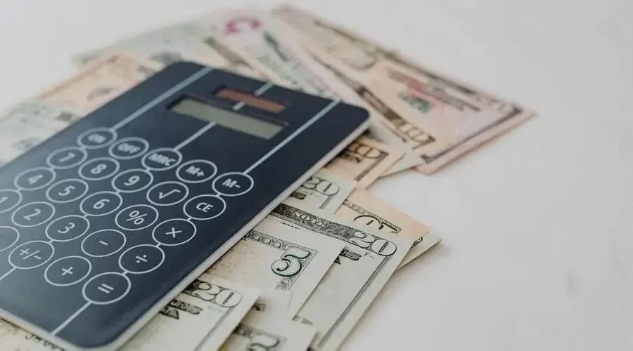 A close-up of a calculator and US dollar banknotes, symbolizing financial calculation and budgeting.