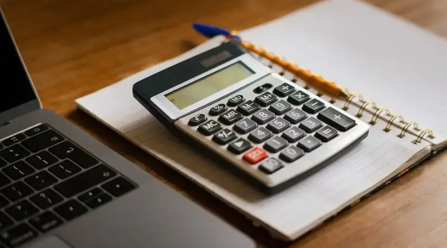 Calculator and open laptop on wooden desk, ideal for financial or accounting tasks.
