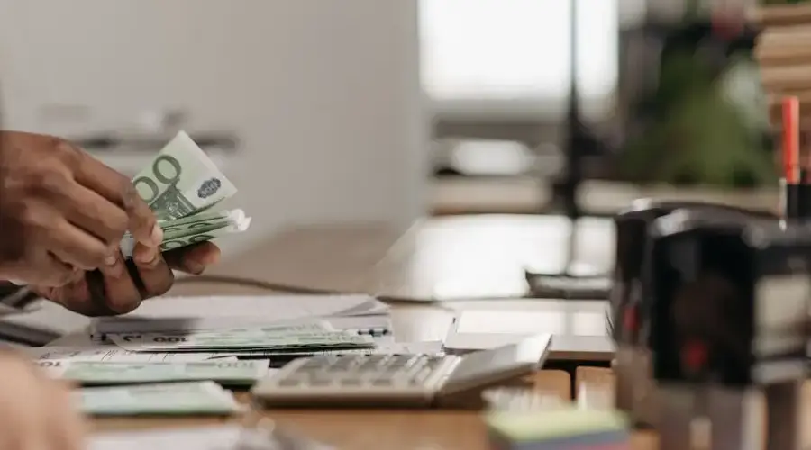 Close-up of hands counting euro bills at an office desk with a calculator.