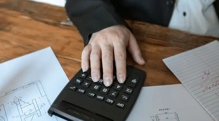 Hand using calculator for architectural calculations on blueprints.