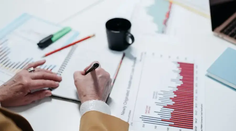 Close-up of hands writing in a notebook surrounded by business charts and documents.