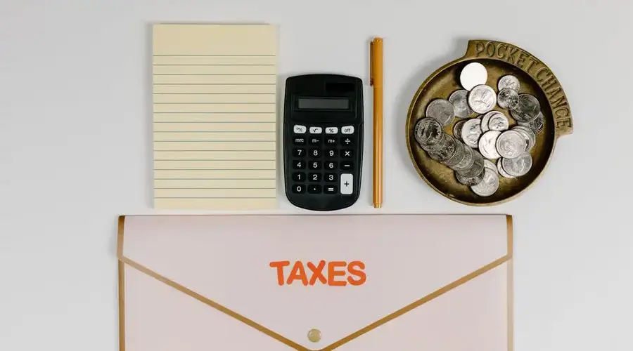 A flat lay of tax preparation essentials: calculator, coins, notepad, pen, and folder.