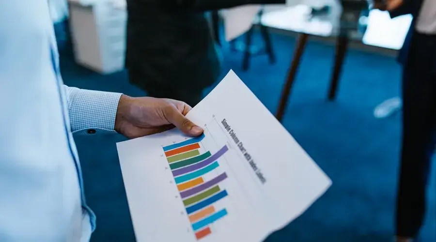 Business personnel reviewing a colorful bar chart report in an office setting.