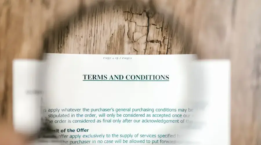 Magnifying glass focusing on terms and conditions document on wooden surface.