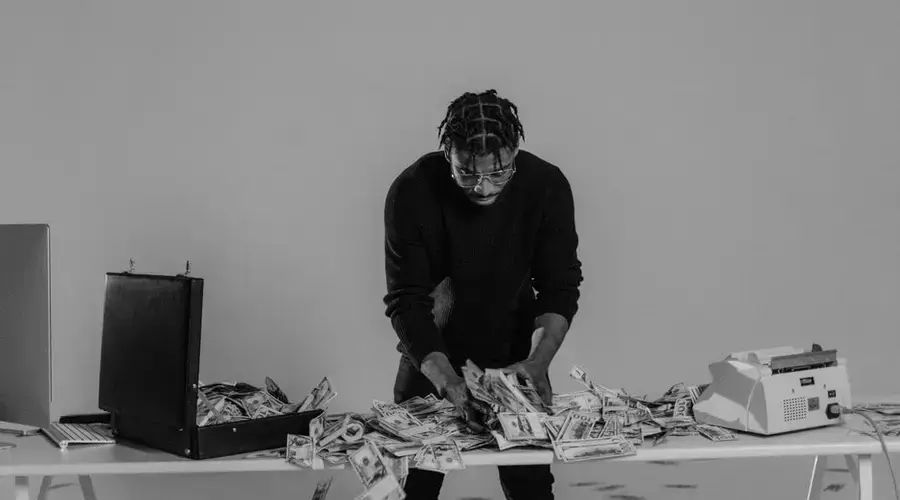Black and white photo of a man sorting cash on a table with a briefcase.