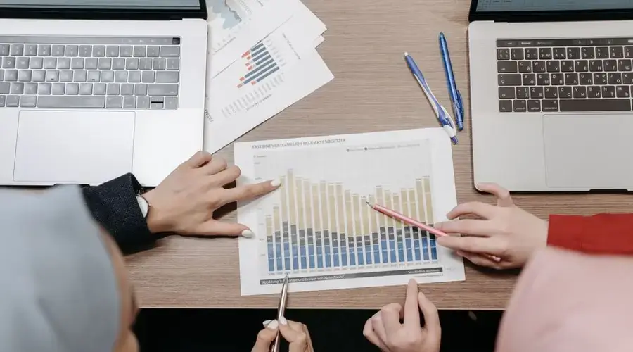 Two individuals analyze sales data and graphs on laptops at a meeting.