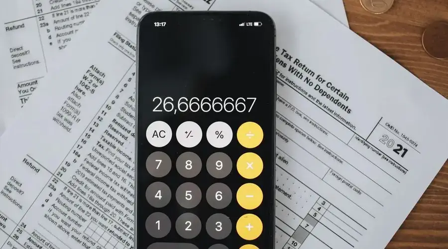 Smartphone calculator over tax forms with coins, symbolizing tax calculation and finance.