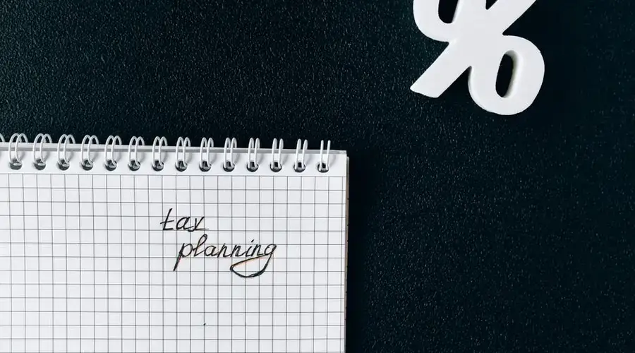 A notebook with 'tax planning' written on a grid paper next to a percent symbol on a black background.