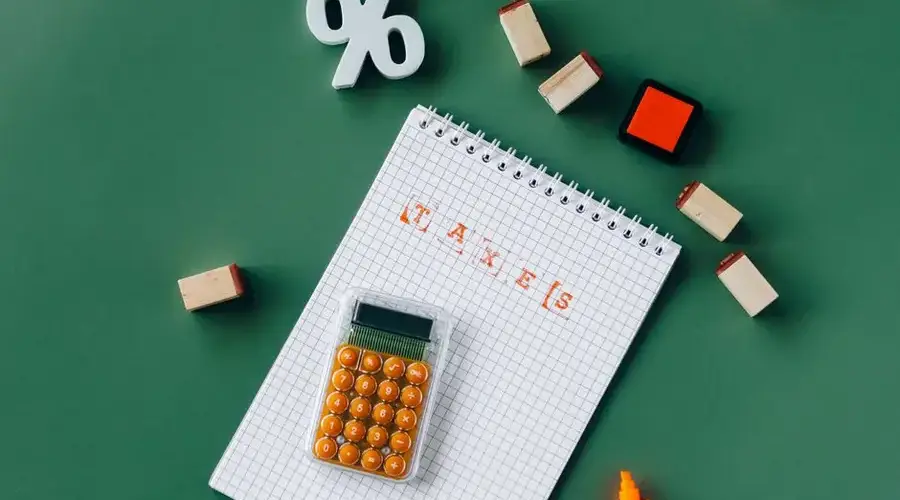 Flat lay of tax essentials with calculator, notebook, and stamps on a green background.