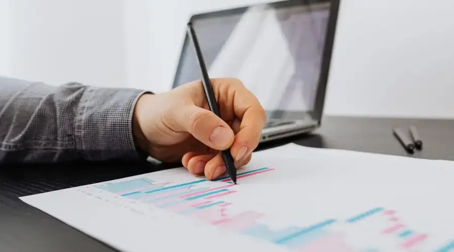 Person taking notes on a business chart with a laptop in the background.