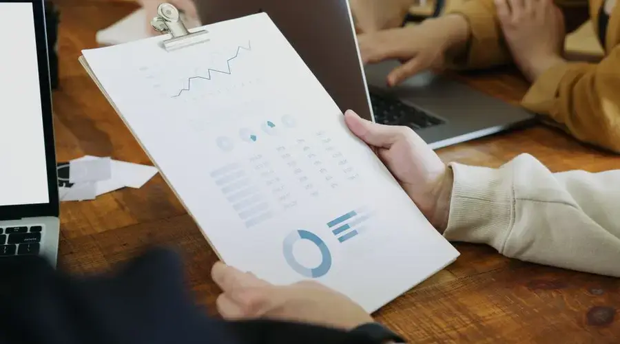 Close-up of hands holding a clipboard with charts and graphs in a business meeting.