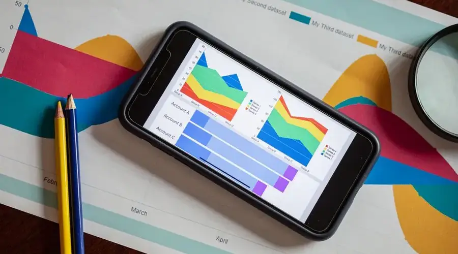 Overhead view of a smartphone displaying colorful charts on paper graphs, symbolizing mobile data analysis.