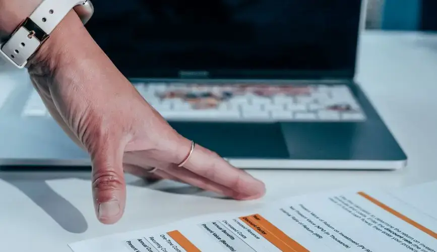 Close-up of a hand reviewing a financial report on a laptop, indicating focus on business analysis.
