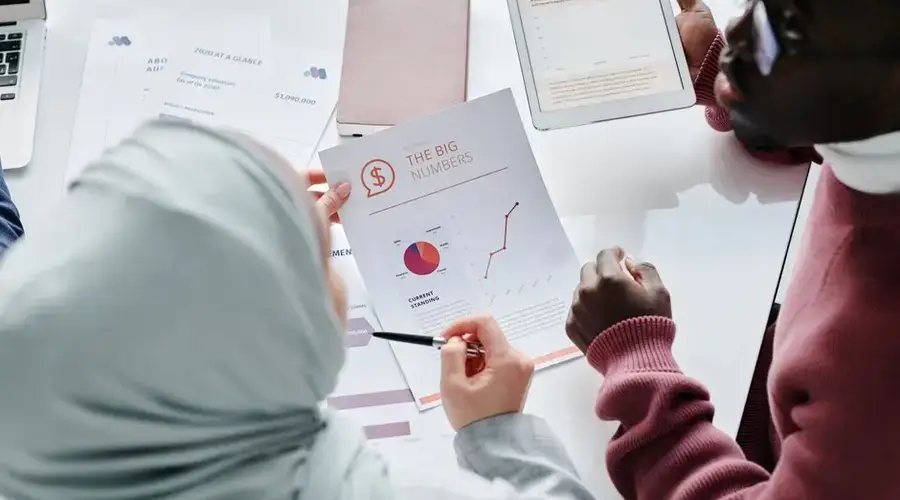 Two colleagues reviewing financial documents and graphs during an office meeting.