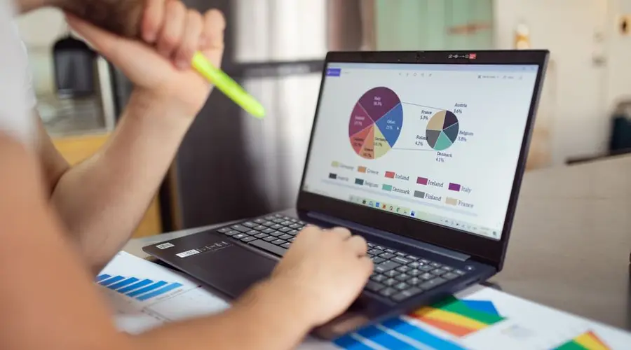 Person analyzing financial charts and graphs on a laptop with colorful documents, showcasing market analysis.