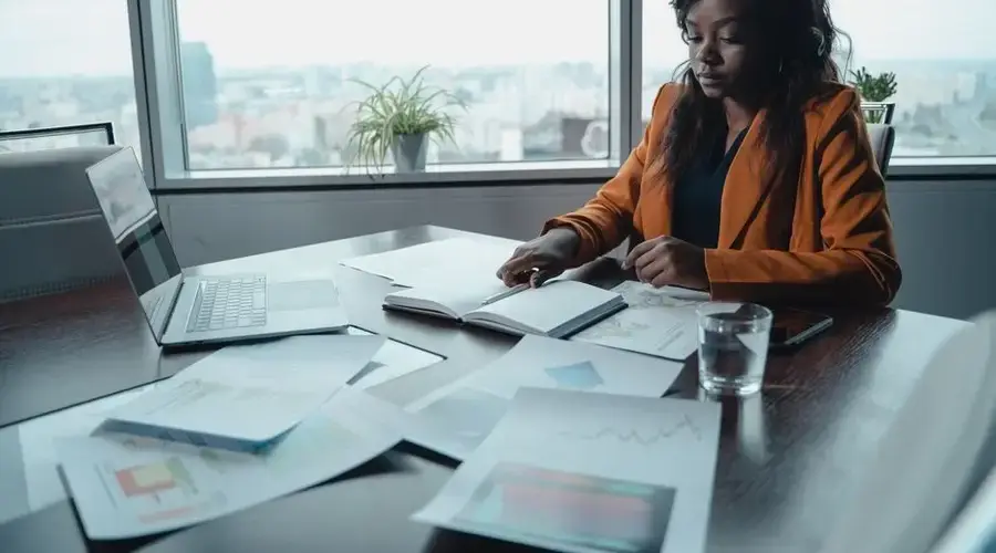 Focused businesswoman reviewing documents at a modern office desk with a city view.