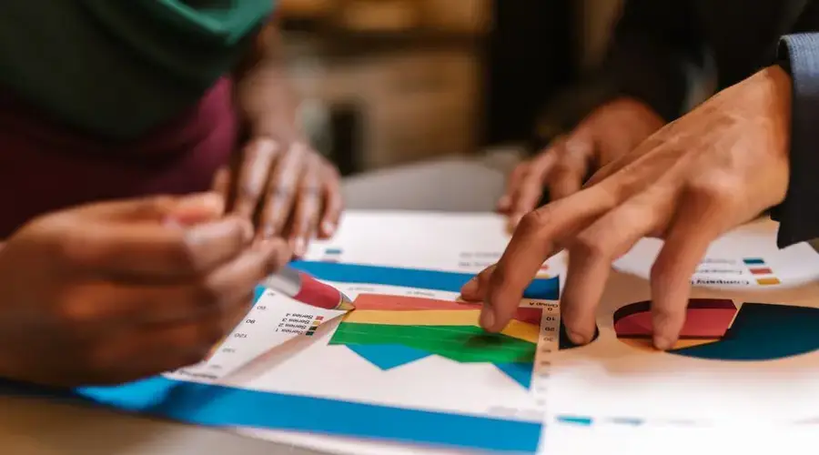 Close-up of hands during a collaborative office meeting analyzing colorful graphs and documents.