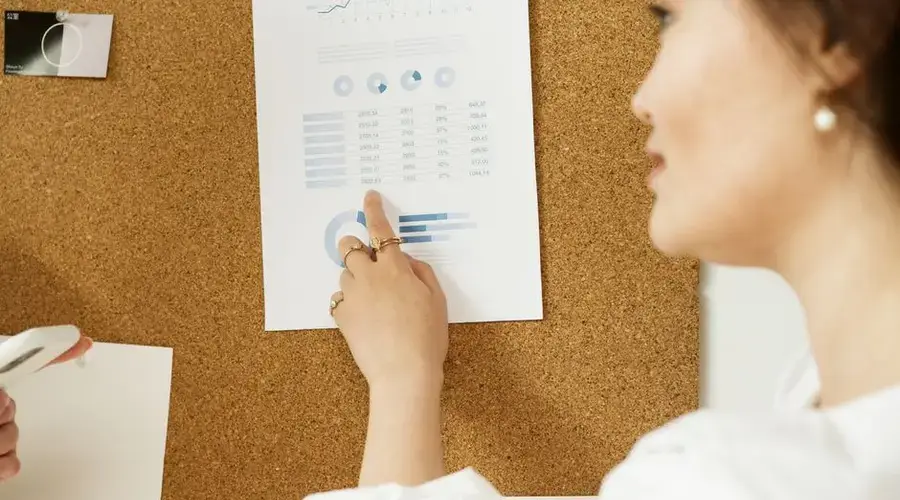 A person pointing at a graph on a cork board during a presentation.