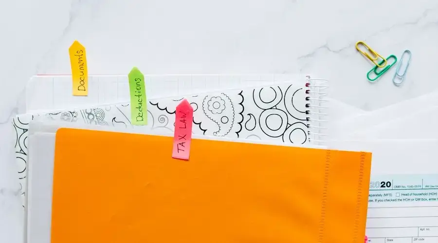 Top view of tax documents organized with colorful sticky notes on a marble desk.