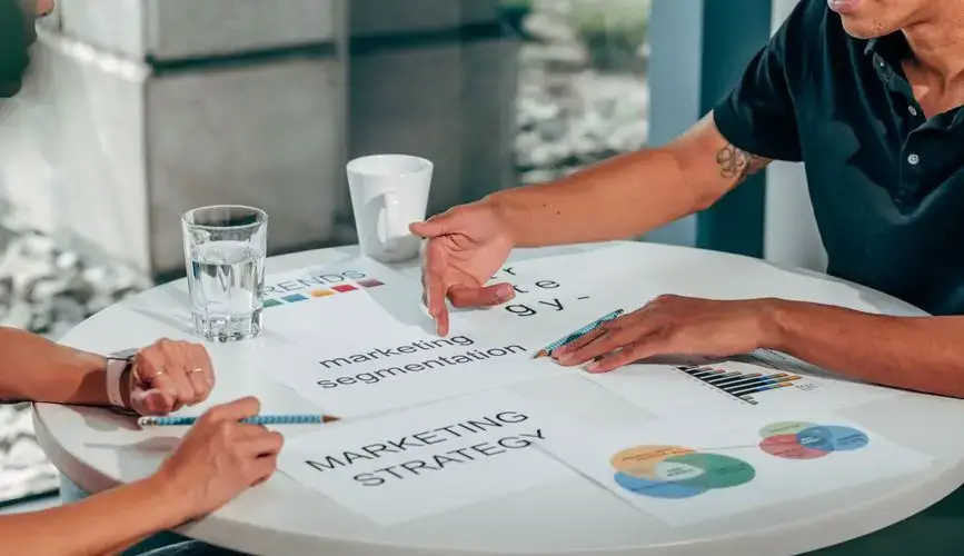 Two adults in an office discussing marketing strategy around a round table.