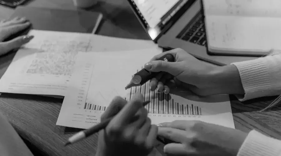 Monochrome image of hands analyzing documents and charts in an office setting.