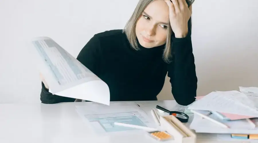 A woman showing stress while reviewing multiple paperwork and financial documents at a desk.