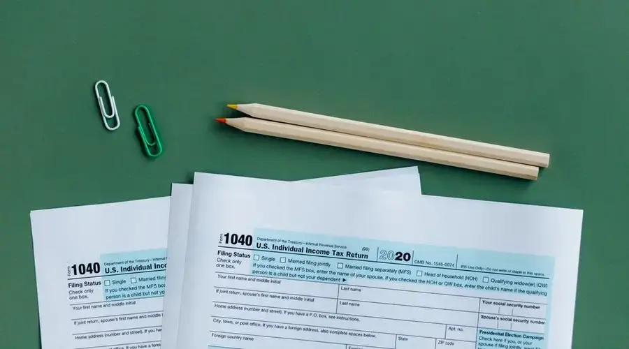 U.S. tax forms with pencils and paperclips on green surface in a flat lay setup.