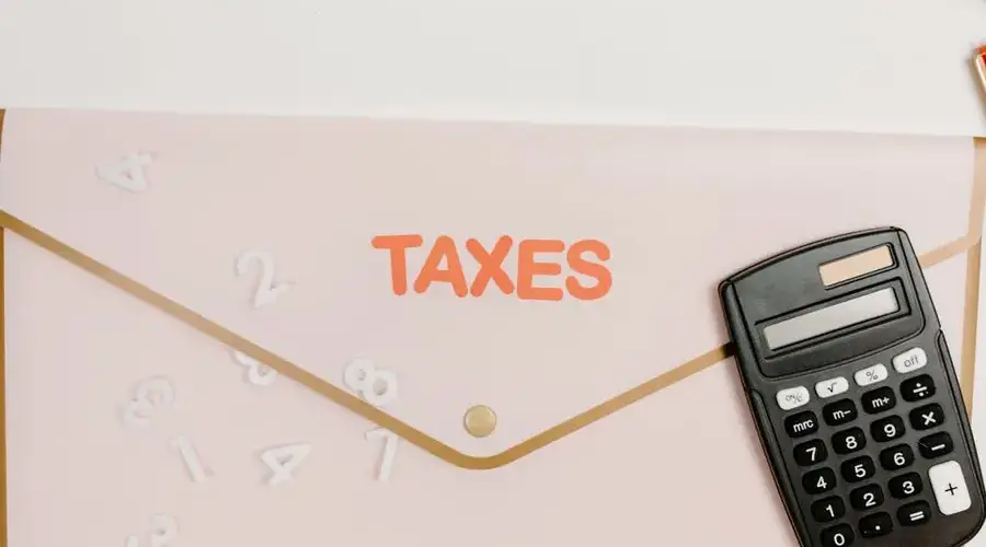 Flat lay of a calculator and folder labeled 'Taxes' for finance and accounting.