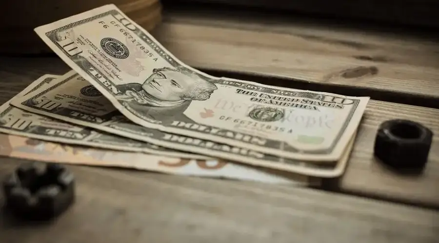 A stack of US dollar bills on a rustic wooden table close-up view.
