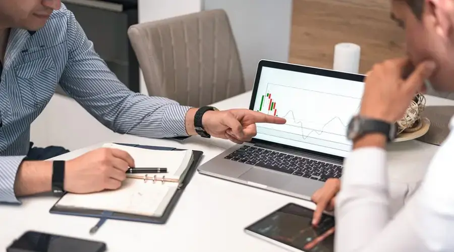 Two businessmen analyzing financial charts and data on a laptop and tablet.