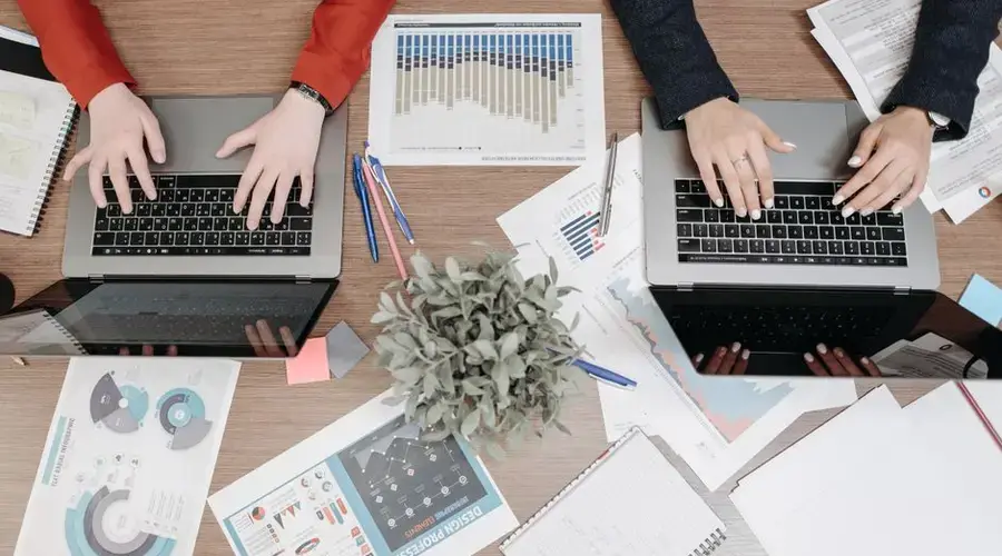 High-angle view of colleagues working on laptops with reports and charts in an office setting.