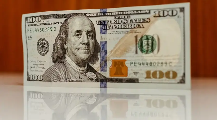 Crisp image of a $100 bill standing and reflecting on a smooth surface, highlighting details.