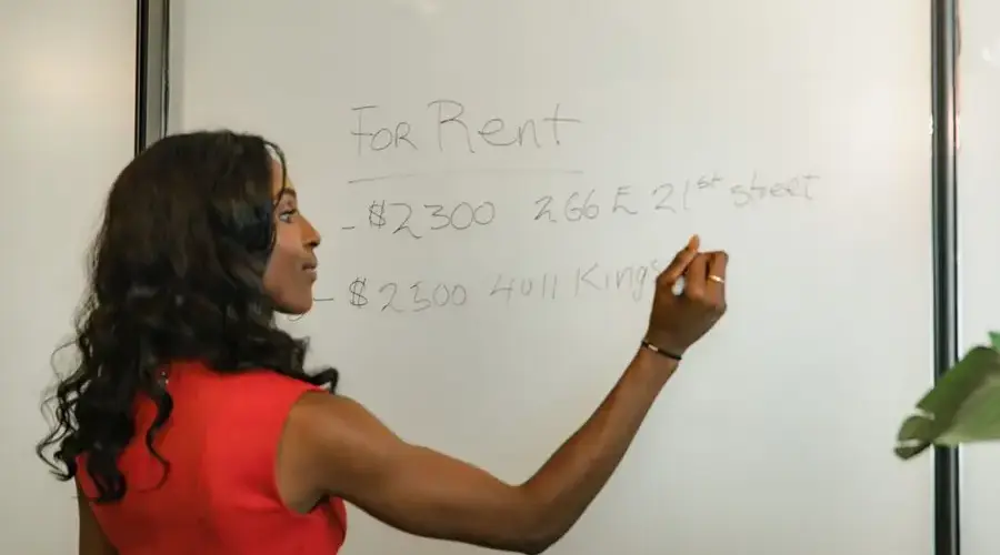 Professional woman writing real estate prices on a whiteboard for rental properties.