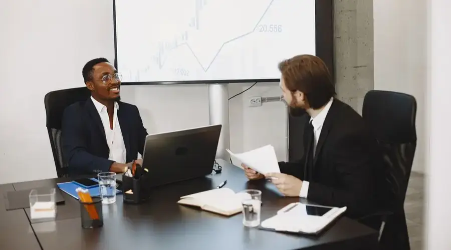 Two businessmen in a professional meeting discussing data on a large screen in a modern office.
