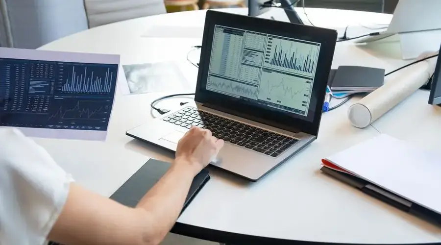 Business person evaluating financial charts on a laptop in a modern office setting.