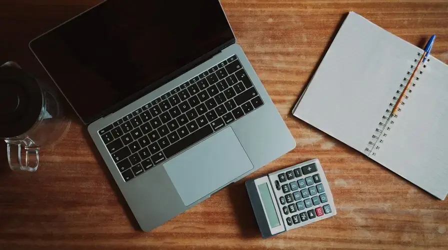 Top view of a desk with a laptop, calculator, and open notepad for work or study.