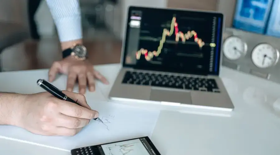 Hands analyzing data on paper alongside a laptop and smartphone showing charts.